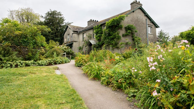 Hill Top house in spring, with a winding garden path bordered by flowering plants and greenery.